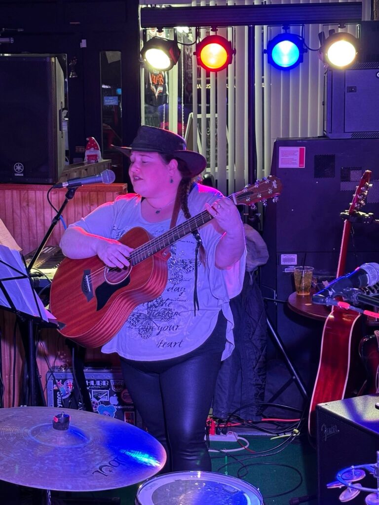 Bobbie JoEle plays guitar in a crowded bar with stage lights behind her.